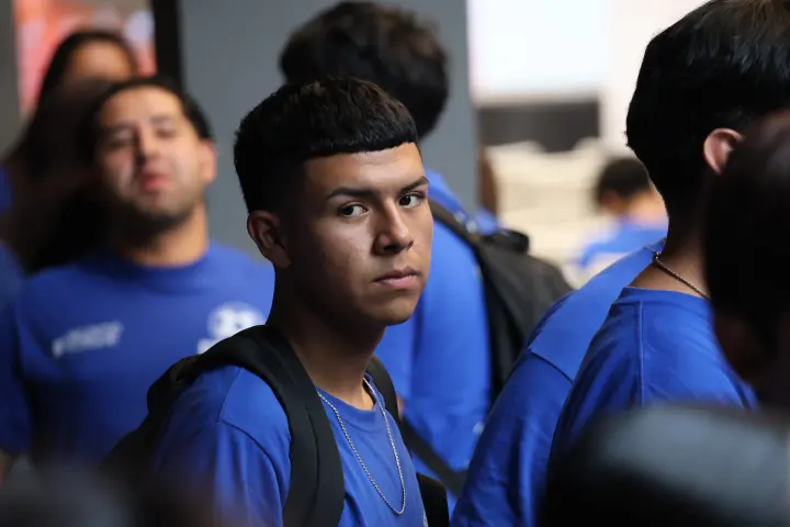 Un joven mira a la cámara entre otros participantes con playera azul