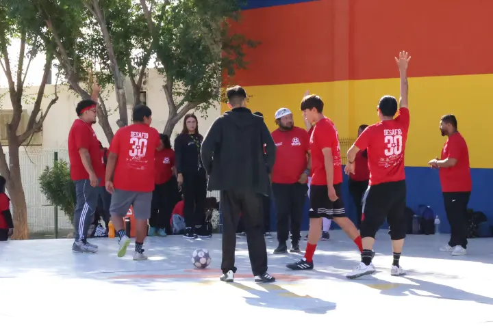 Jóvenes con playera roja juegan fútbol en una cancha